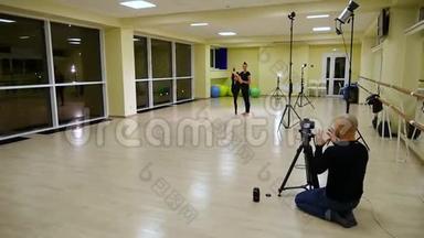 视频摄影师拍摄为两个苗条可爱的女孩姐妹艺术体操运动员穿黑色运动服在健身房热身。